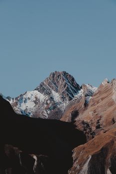 A stunning view of a rocky mountain peak with snow-covered slopes under a clear blue sky.