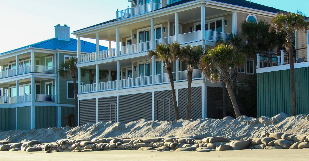 Contemporary beachfront villas with palm trees lining the sandy shore under a clear sky.