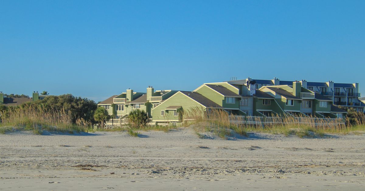 Charming beachfront condos surrounded by dune grass on a sunny day. Perfect for coastal living themes.