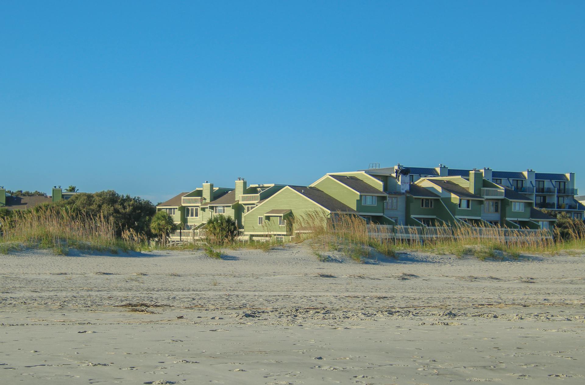 Charming beachfront condos surrounded by dune grass on a sunny day. Perfect for coastal living themes.