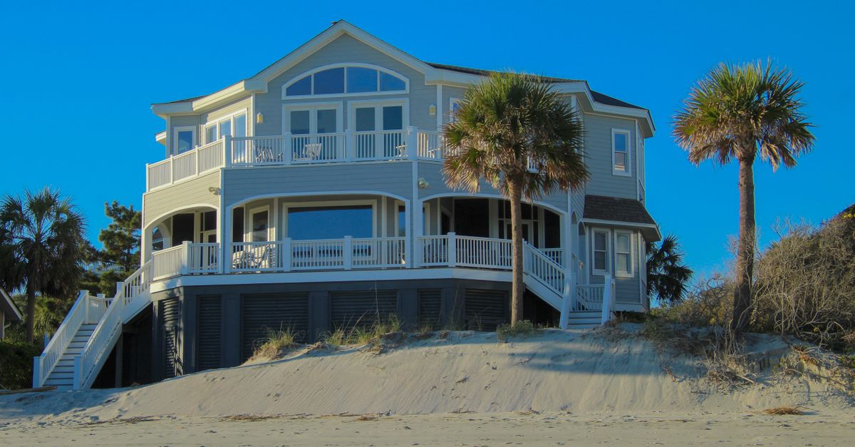 Elegant beachfront house with large windows and palm trees under clear blue sky.