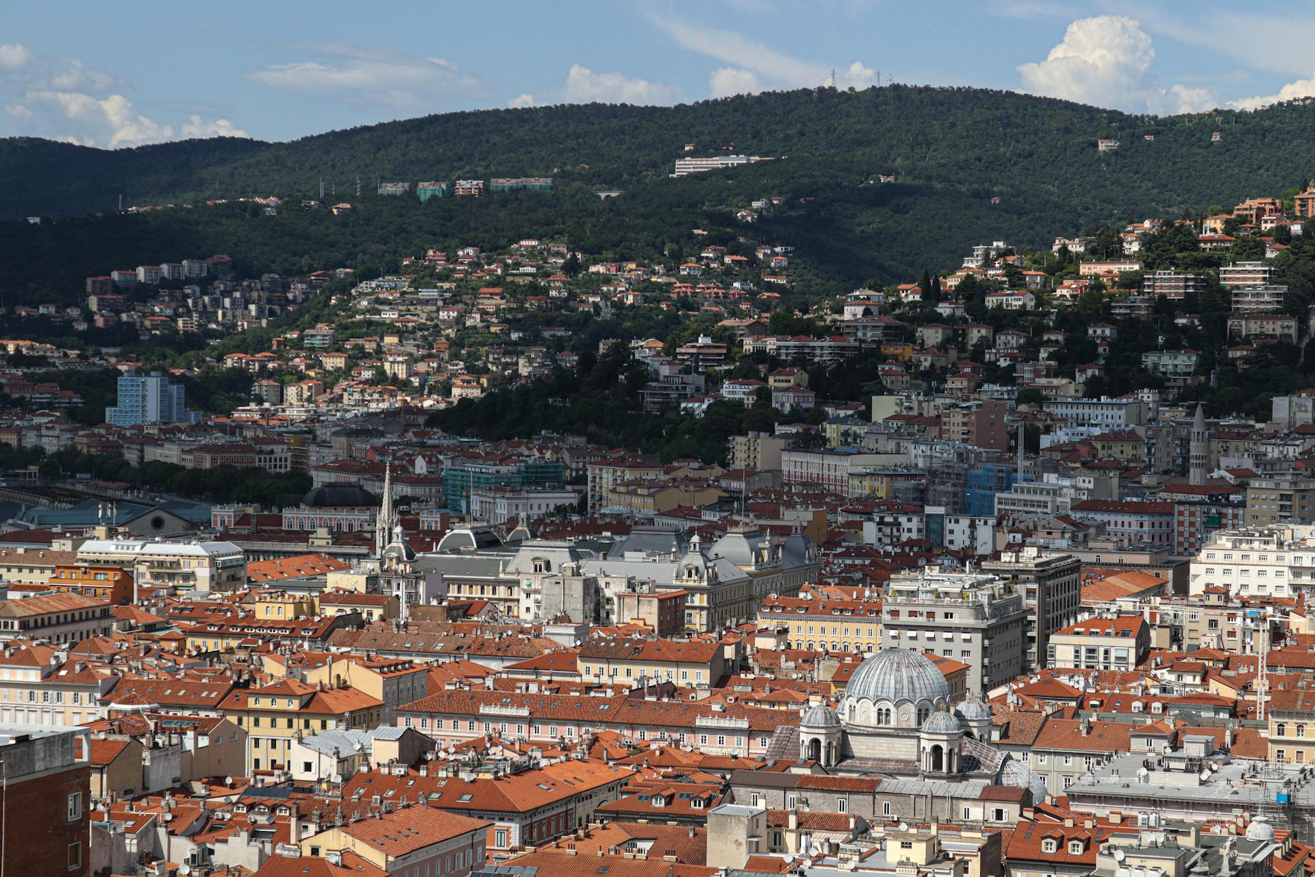 Explore the charming architecture of Trieste from above, showcasing its iconic red rooftops and surrounding hills.