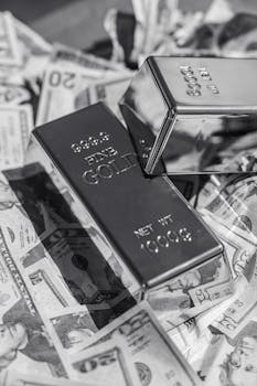 Black and white image of gold bars placed on scattered US dollar bills, symbolizing wealth.