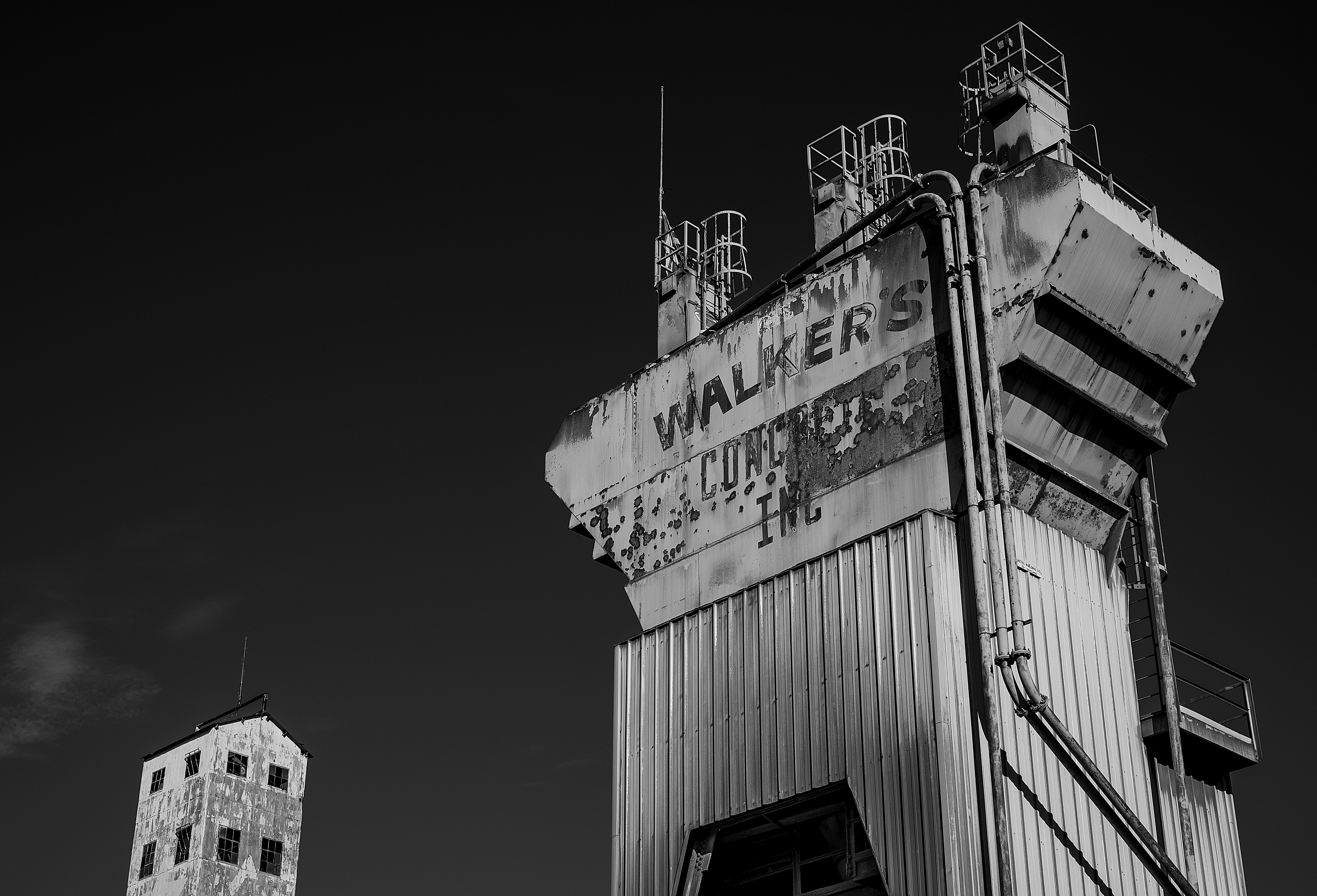 Kostenlos Schwarzweißfoto eines verfallenden Industrieturms mit sichtbarem Text vor einem dunklen Himmel. Stock-Foto