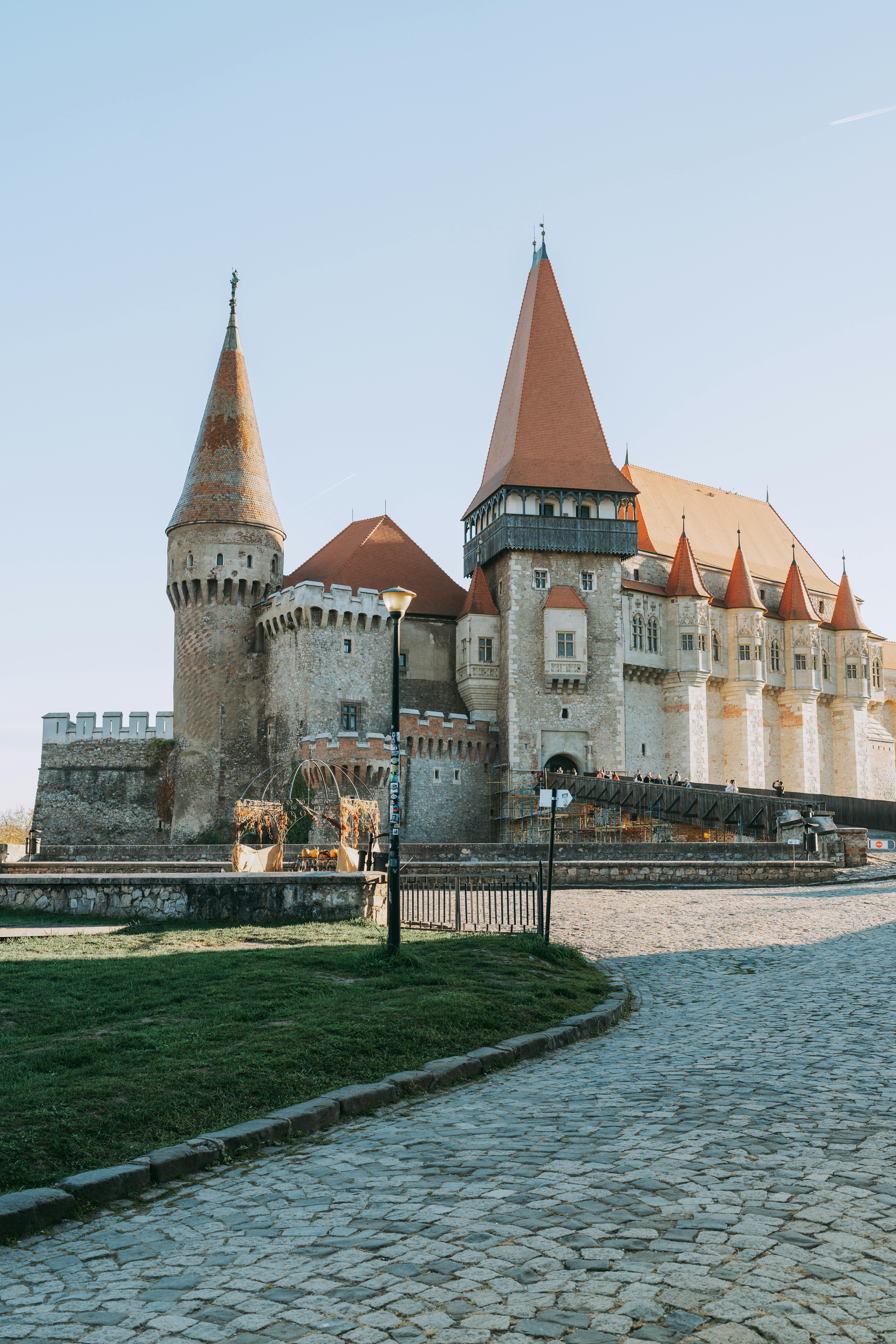 Corvin Castle at golden hour with Gothic spires, Transylvanian countryside, and moat views glowing in warm morning light