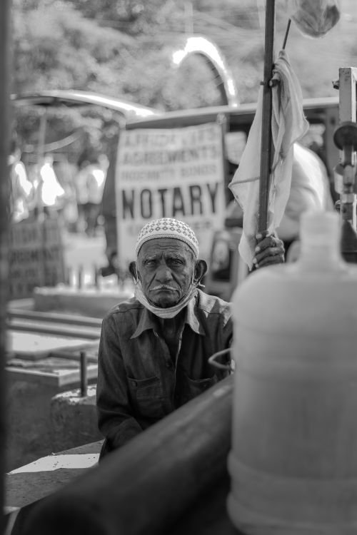 Free Elderly man sitting in a marketplace, wearing traditional attire, with signage in the background. Stock Photo