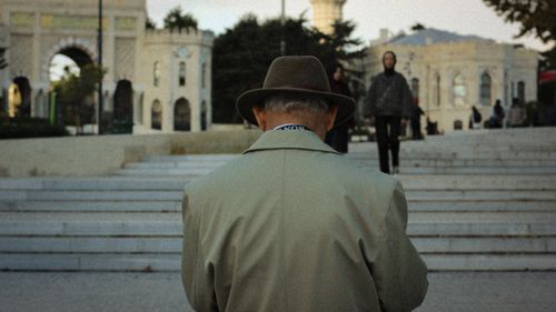 Free An elderly man in a hat stands on steps before a grand historical building. Stock Photo