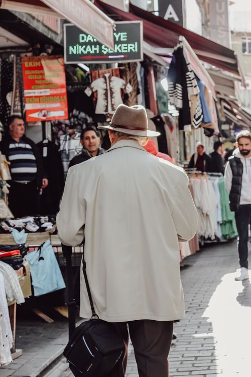 Free Elderly man in a hat wandering through a vibrant street market on a sunny day. Stock Photo