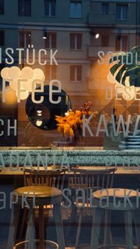 Reflection of a warmly lit coffee shop with chairs outside a window at dusk.