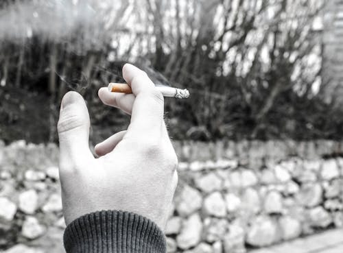 Selective Color Photography of Person Holding Cigarette Stick