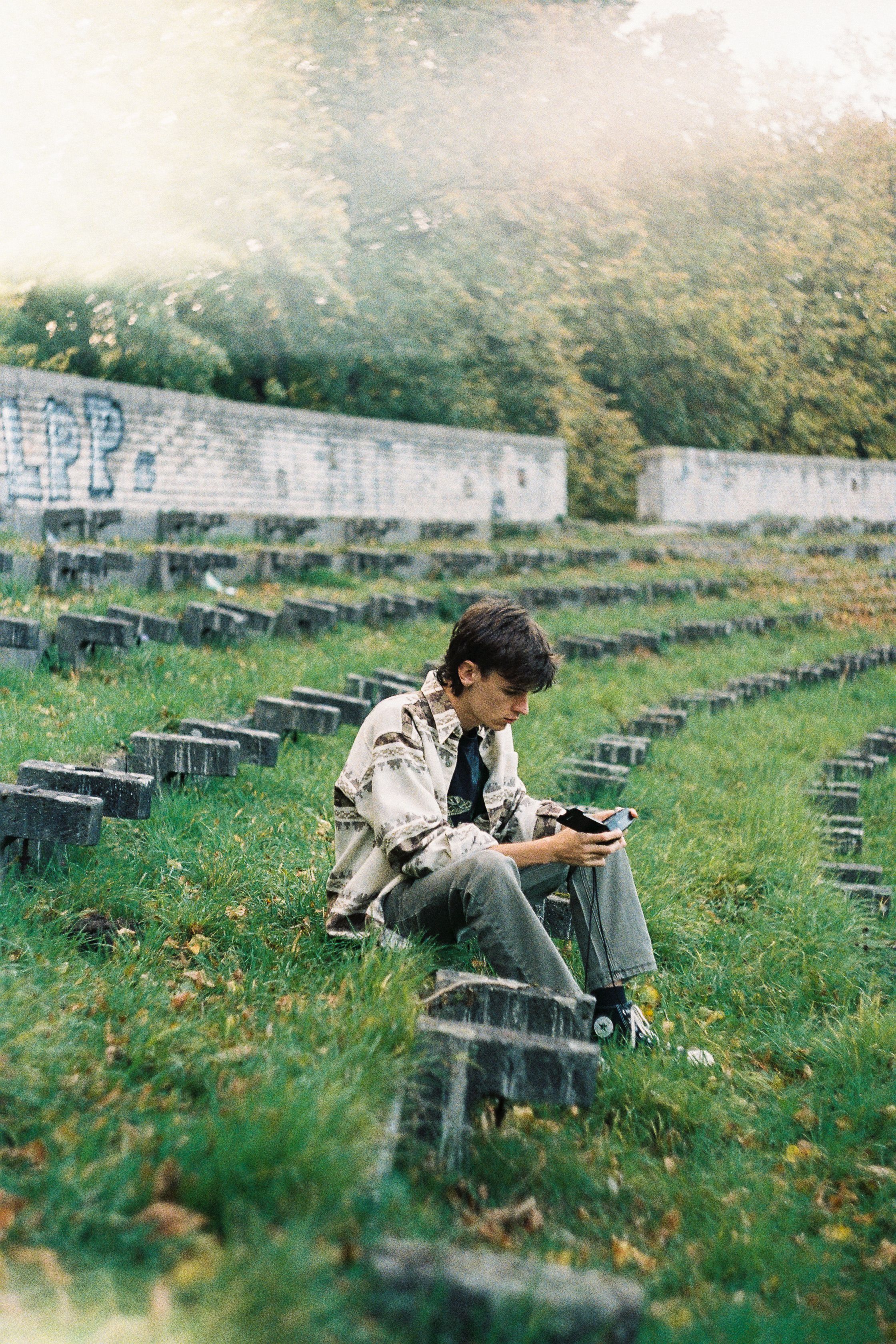 A young man sits in an outdoor amphitheater with a vintage camera. Ideal for urban lifestyle themes.