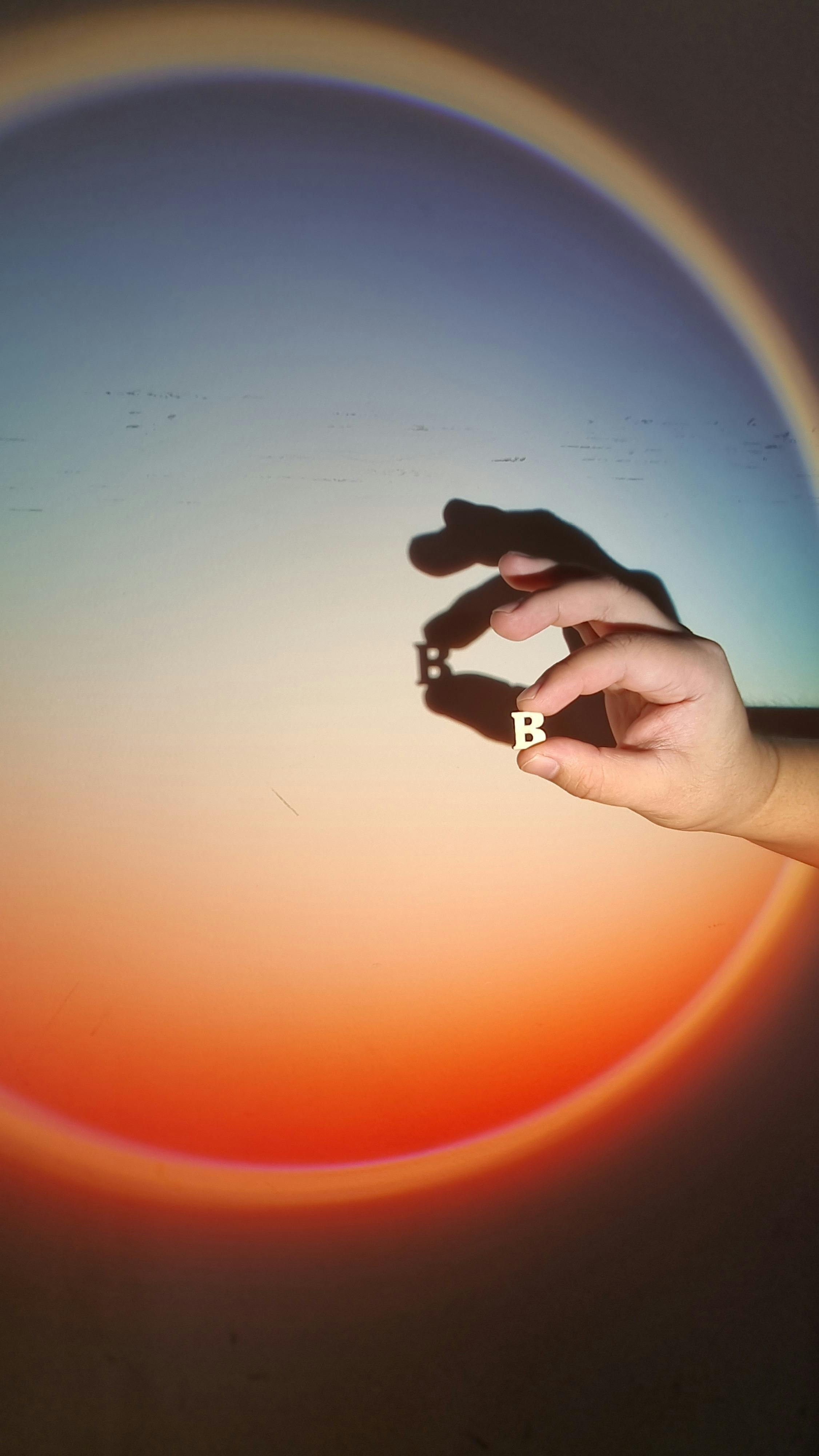 A hand creates a shadow art of the letter B against a gradient circular background.