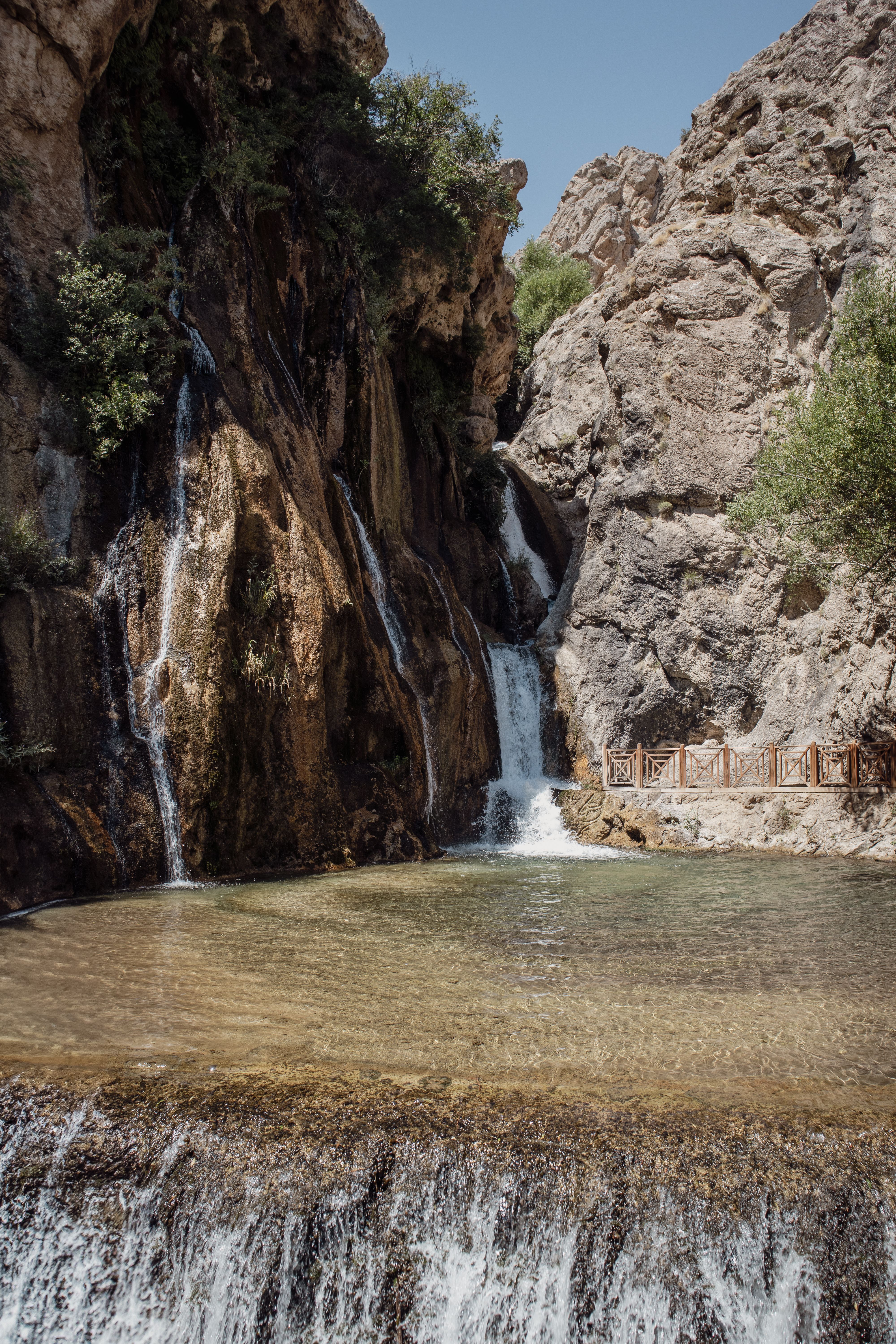 Tranquil waterfall cascading down rocks in Darende, Türkiye, under a bright sky.