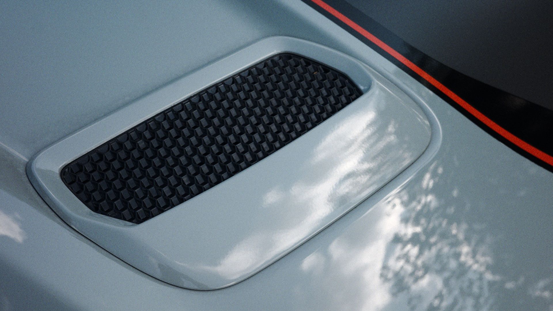 Detailed view of a car hood vent featuring a red racing stripe, exuding a sporty feel.