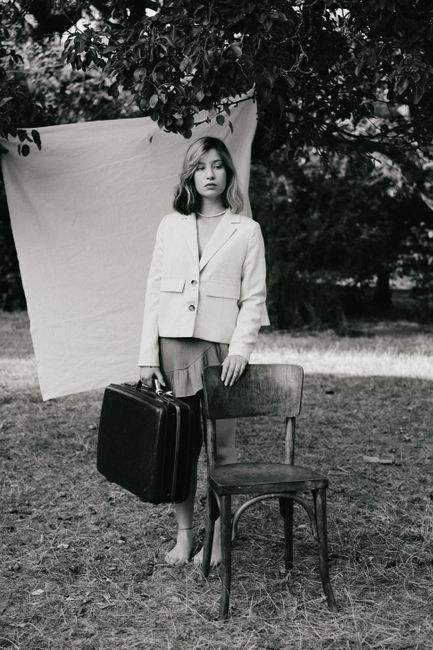 Stylish black and white portrait of a woman holding a suitcase in an outdoor setting.