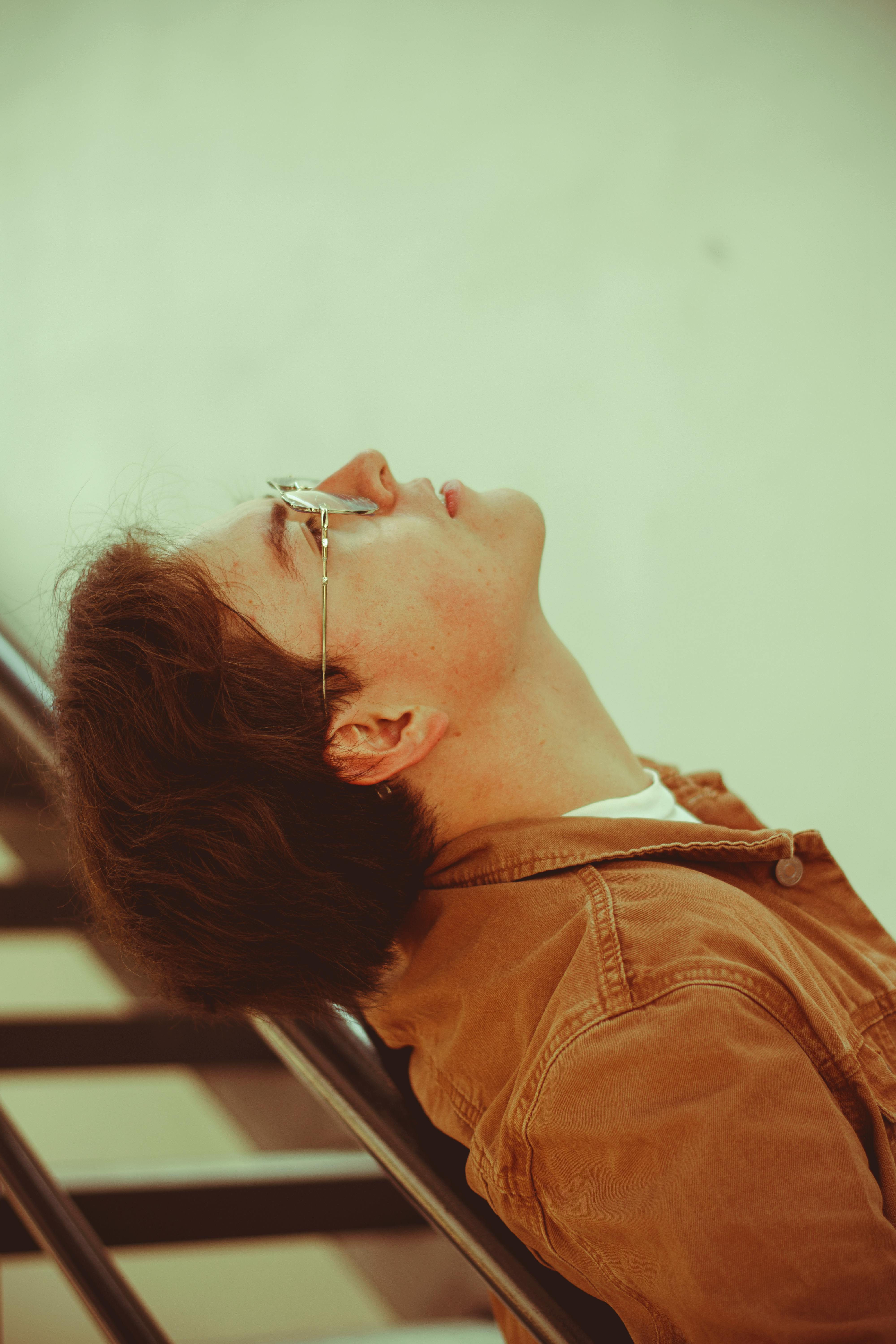 A thoughtful young man in glasses leans on a staircase, deep in contemplation.