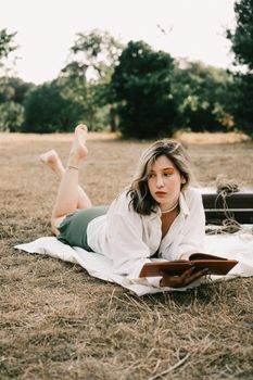 Young woman lying on blanket reading a book outdoors in a serene meadow.