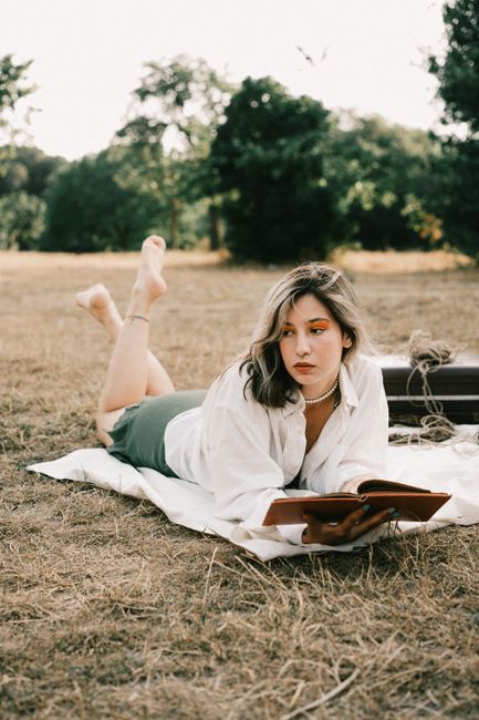 Young woman lying on blanket reading a book outdoors in a serene meadow.