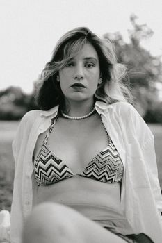 Black and white photo of a woman in a zigzag bikini and white shirt outdoors.