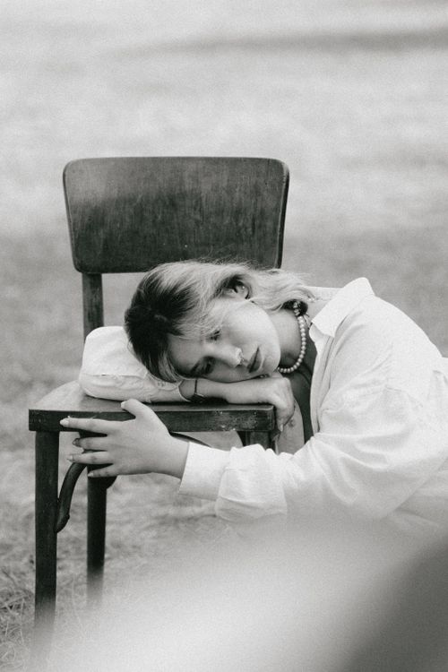 Free Black and white photo of a pensive woman resting her head on a chair outdoors. Stock Photo