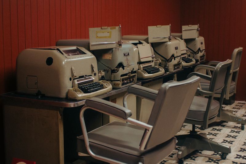 A nostalgic look at a row of vintage typewriters in an office setting with classic chairs.