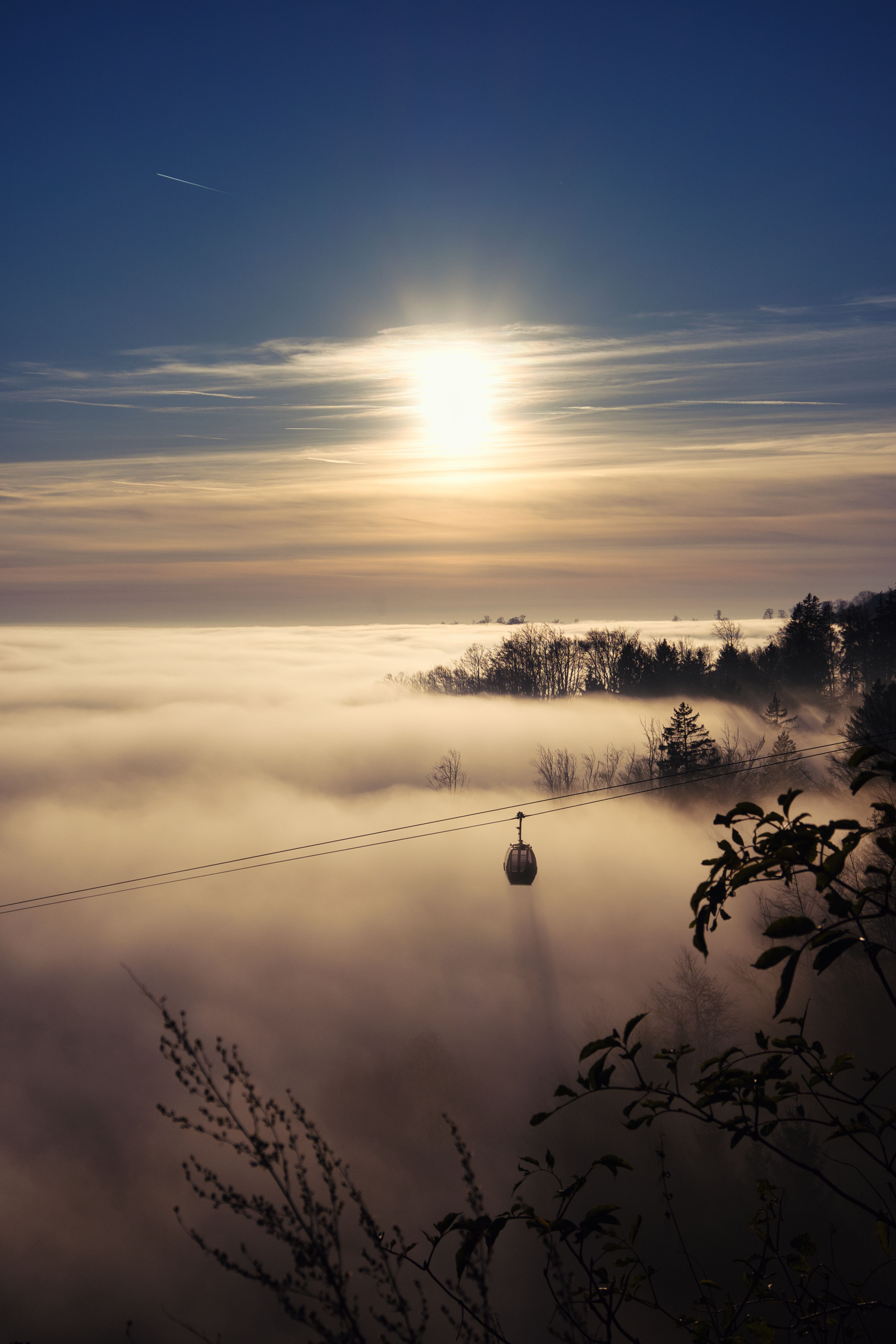 A lone cable car travels through a foggy landscape at sunrise, creating a serene and mystical atmosphere.