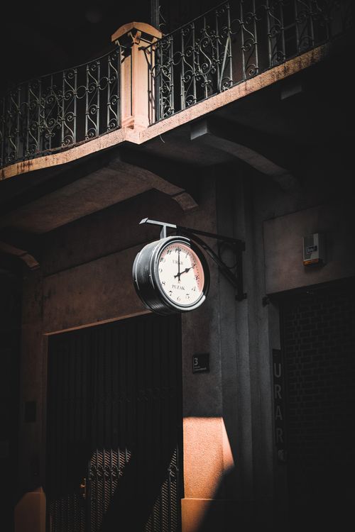 Free A vintage clock hanging on an old building facade, casting shadows. Stock Photo