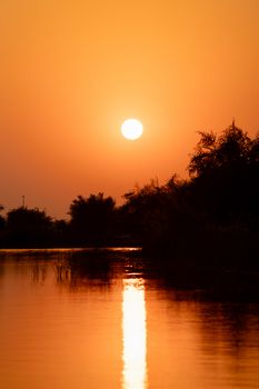 A stunning sunset casting vibrant orange hues over a calm river with silhouetted trees.