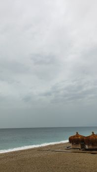 Peaceful beach scene with thatched umbrellas and an overcast sky, conveying a tranquil seaside atmosphere.