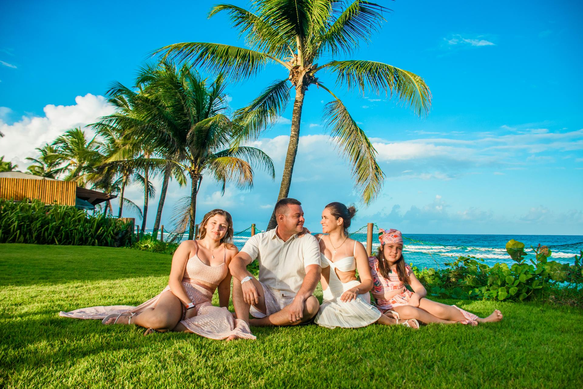 Family enjoying a sunny day on lush green lawn by the ocean with palm trees.