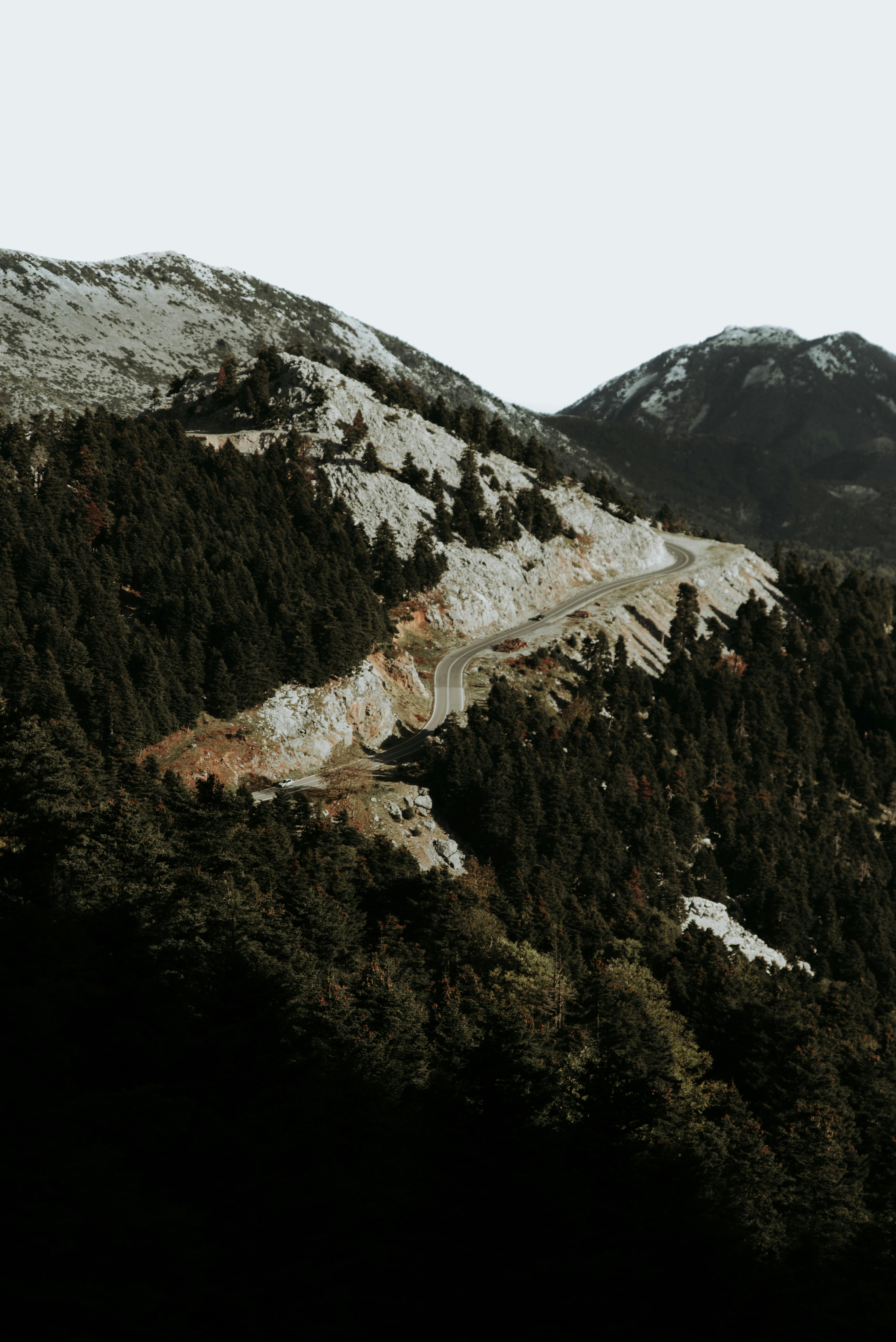 Winding road through a forested mountain landscape under a cloudy sky.
