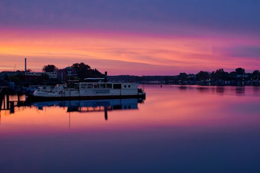 A boat on a peaceful river reflects stunning sunset hues of purple and orange.