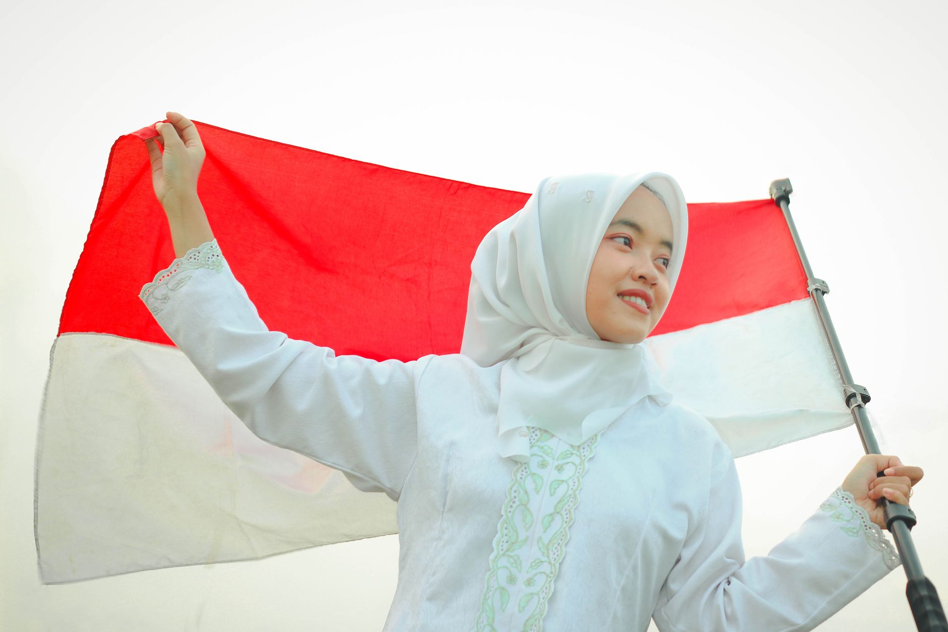 A smiling young woman holds the Indonesian flag, embodying national pride.