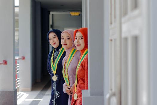 Three young women in hijabs with medals celebrate their academic achievements.