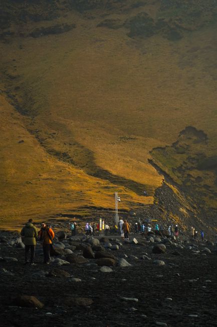 Visitors walk along a beautiful volcanic black sand beach beneath towering hills.