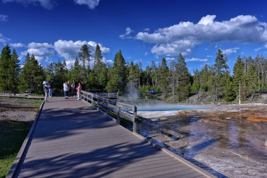 Tourists exploring the geothermal features at Yellowstone's scenic boardwalk under a clear blue sky.