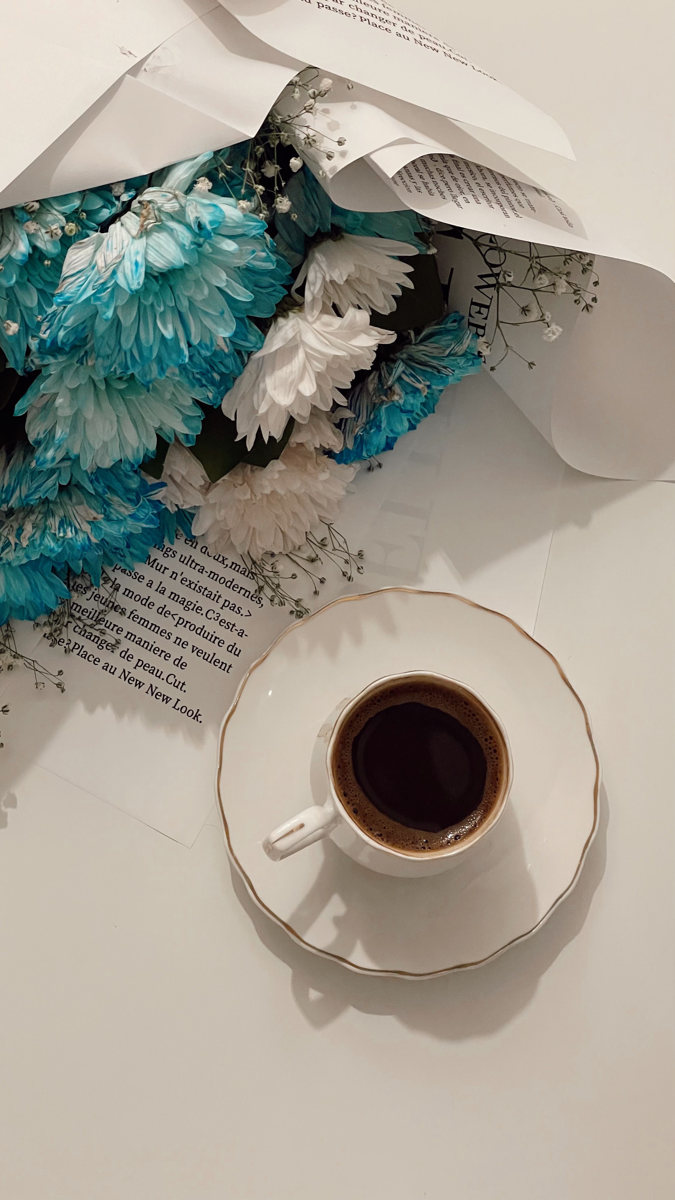 A cup of coffee beside a bouquet of vibrant blue and white chrysanthemums.