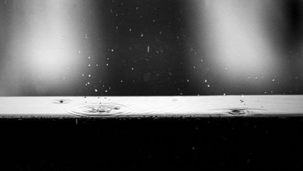 Black and white close-up of water droplets creating ripples on a surface, capturing urban details.