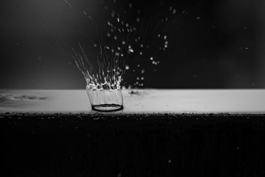 Stunning black and white photograph capturing a water drop impact with detailed splash effect on a surface.