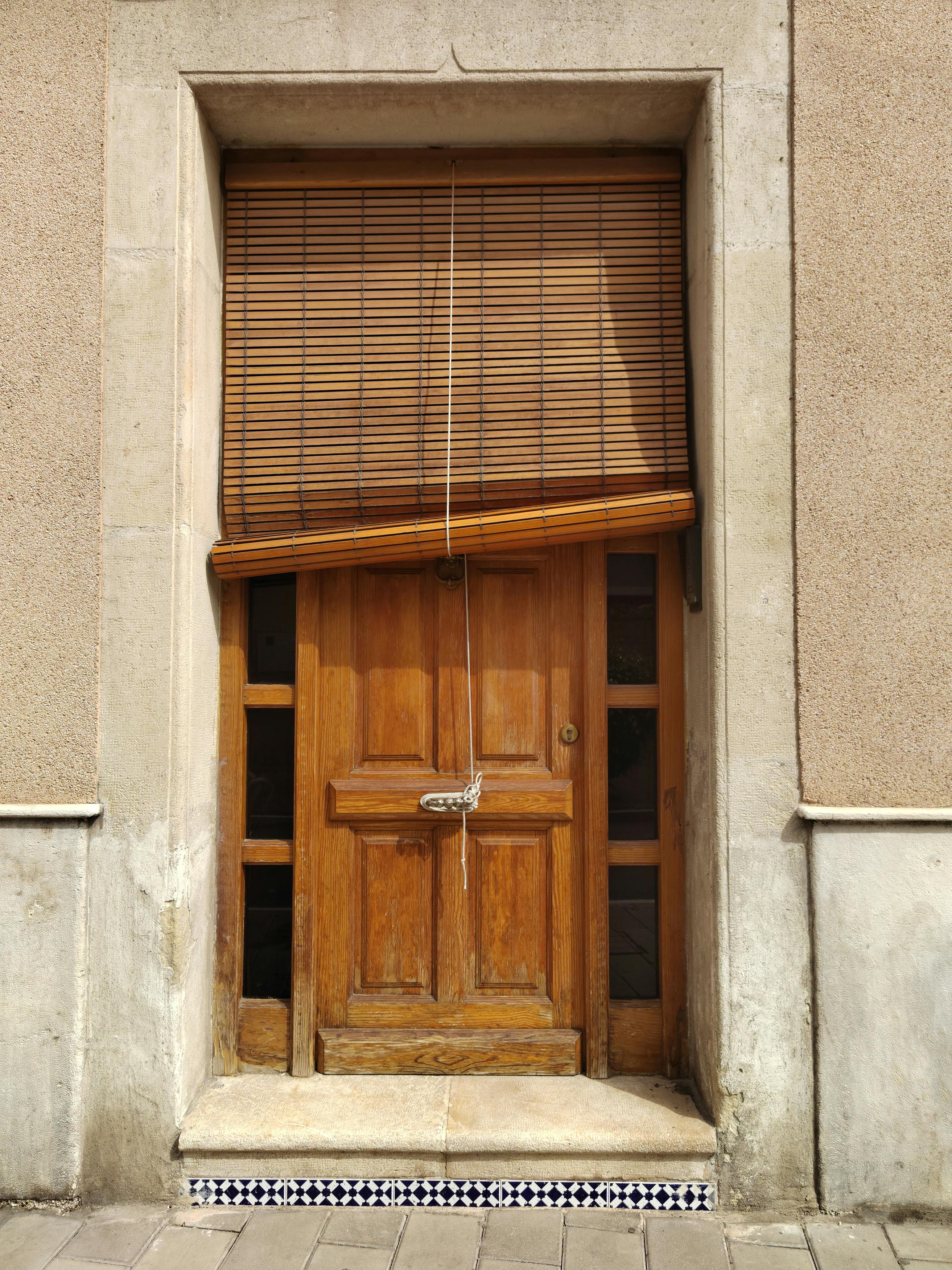 Wooden door framed by brick wall and bamboo blinds, captured in daylight.