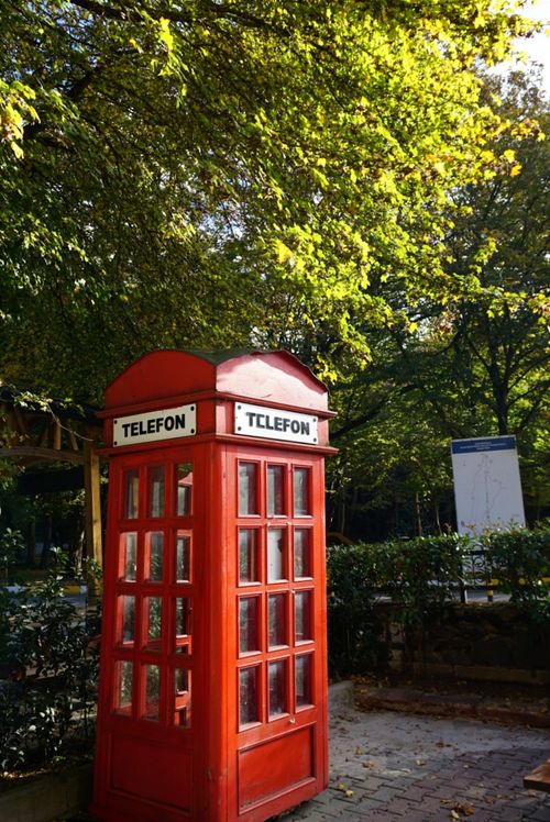 Free Classic red telephone booth in a leafy park setting on a sunny day. Stock Photo