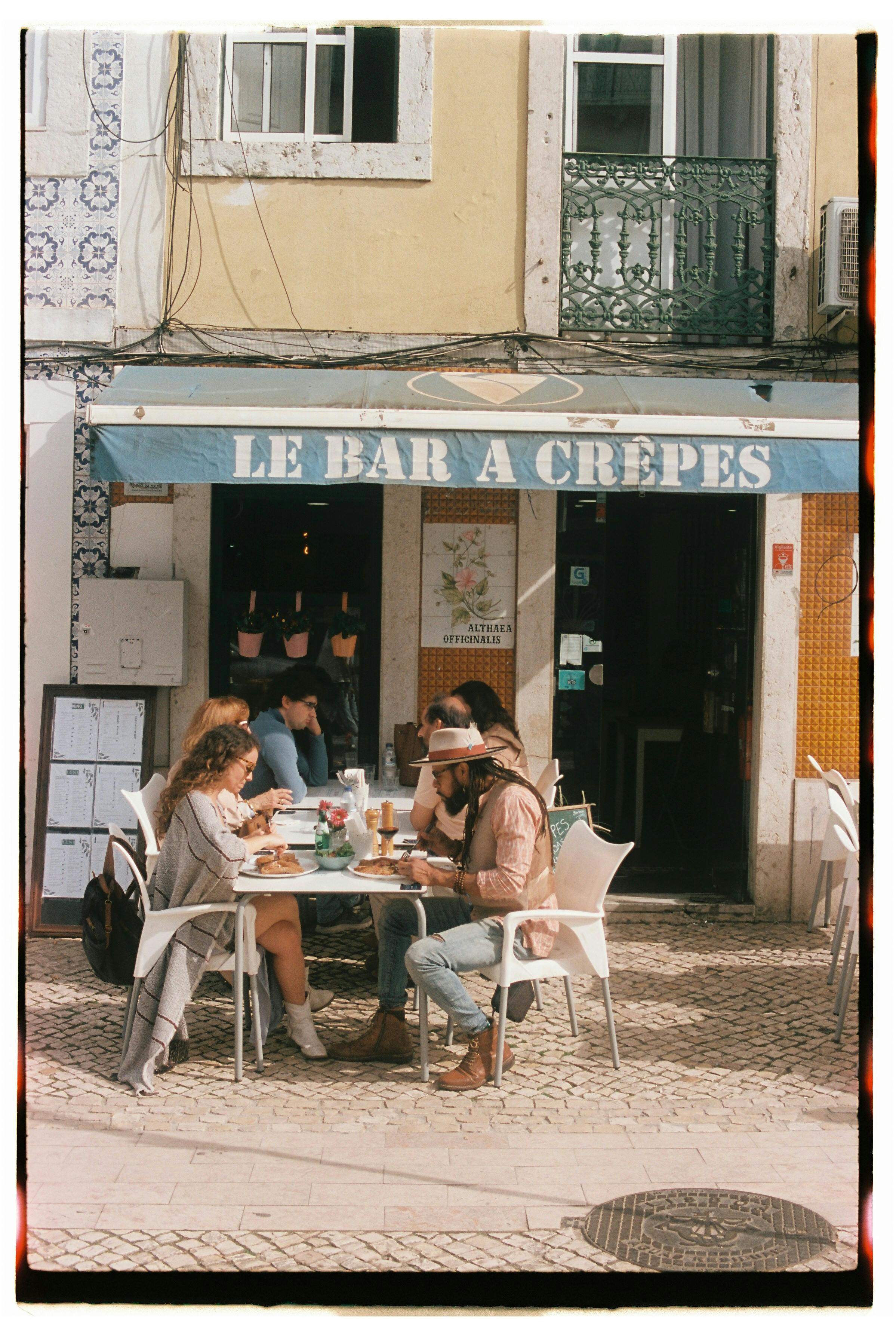 Visitors enjoy outdoor dining at Le Bar à Crêpes in sunny Lisbon, Portugal.