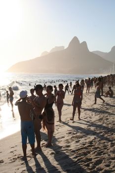 Crowded Ipanema Beach at sunset with people enjoying the ocean and scenery, Brazil.