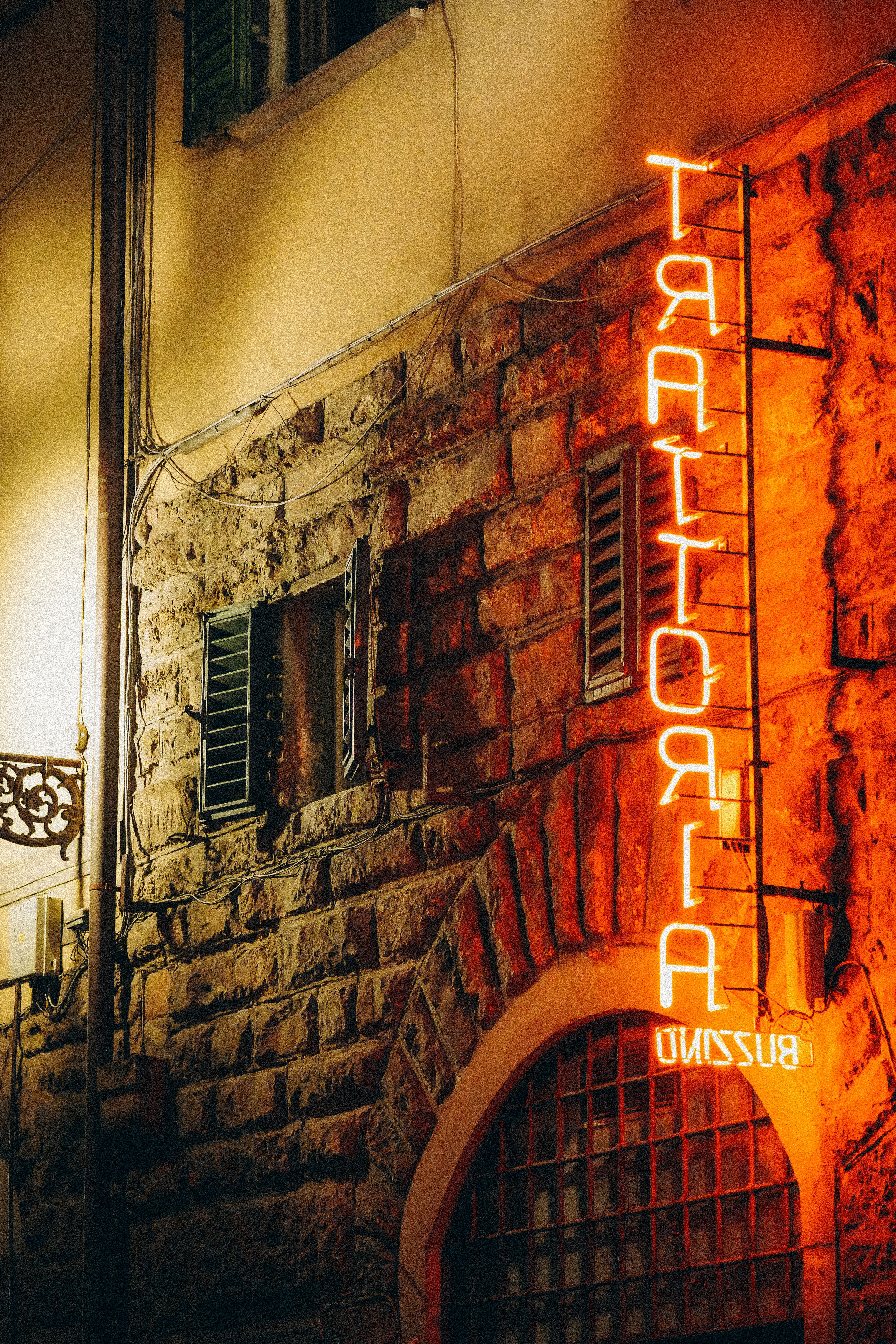 Charming Trattoria Neon Sign on Rustic Stone Wall · Free Stock Photo