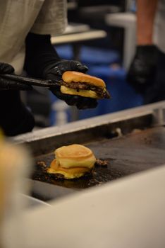 Chef uses tongs to flip delicious beef burgers on a grill inside a restaurant.
