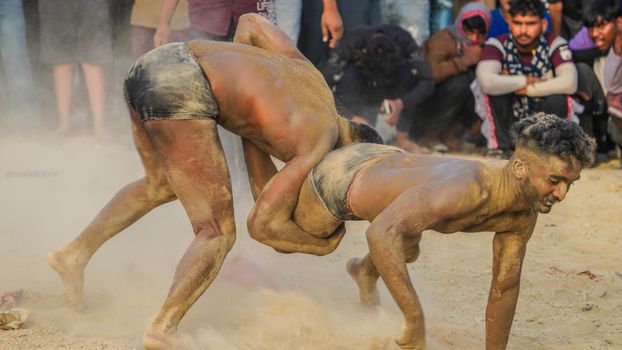 Two men engaged in a traditional wrestling match with an audience watching.