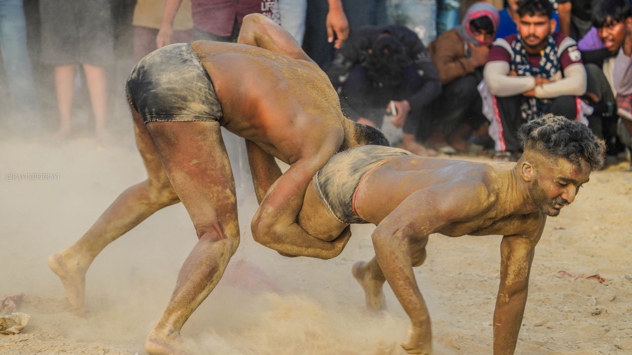 two men engaged in a traditional wrestling match with an audience watc