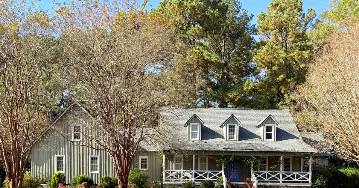 A picturesque ranch-style house surrounded by autumn trees and greenery.