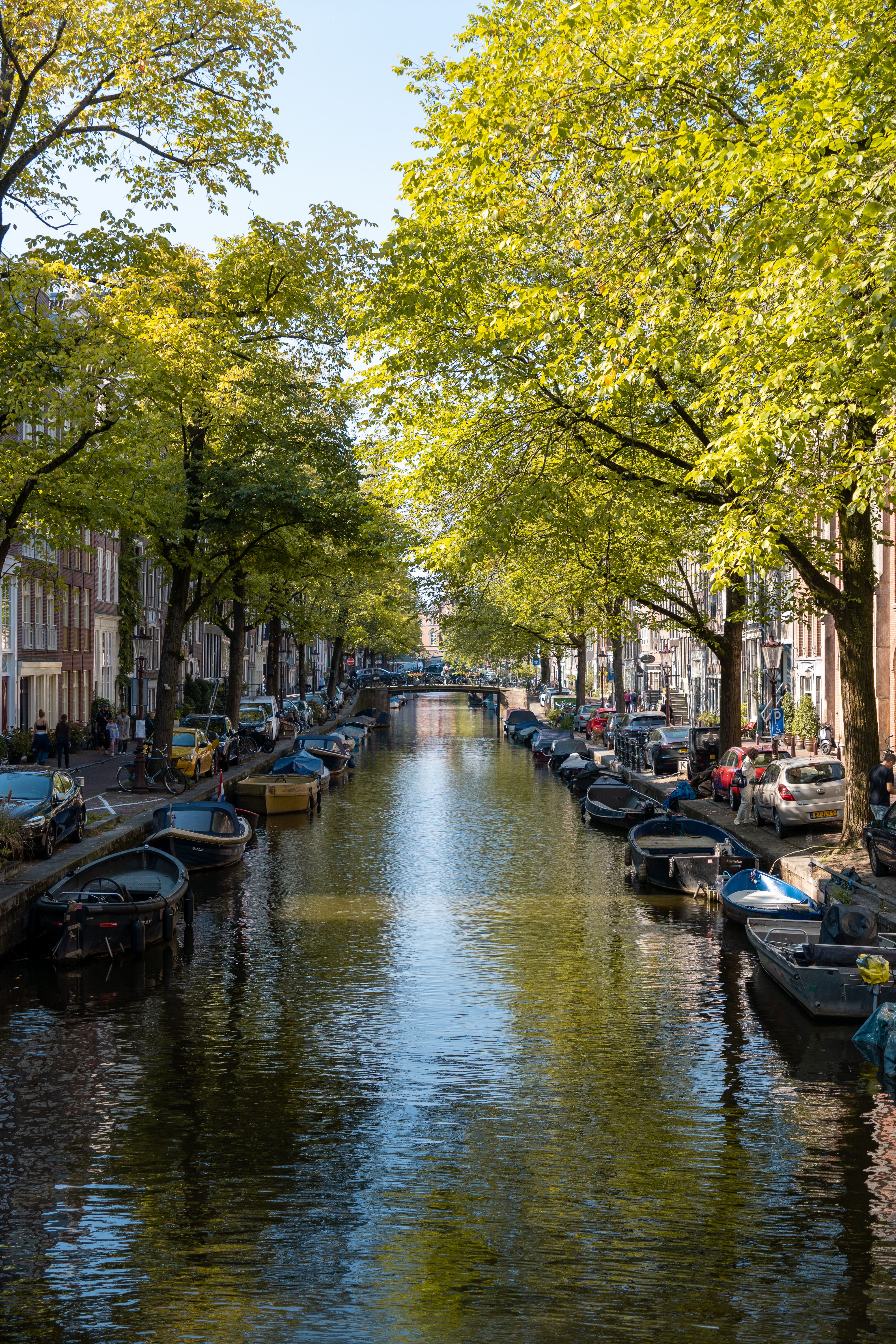 Scenic Amsterdam canal with moored boats and trees, illustrating the compact, cyclable city an Amsterdam dating site English speaker gets to know
