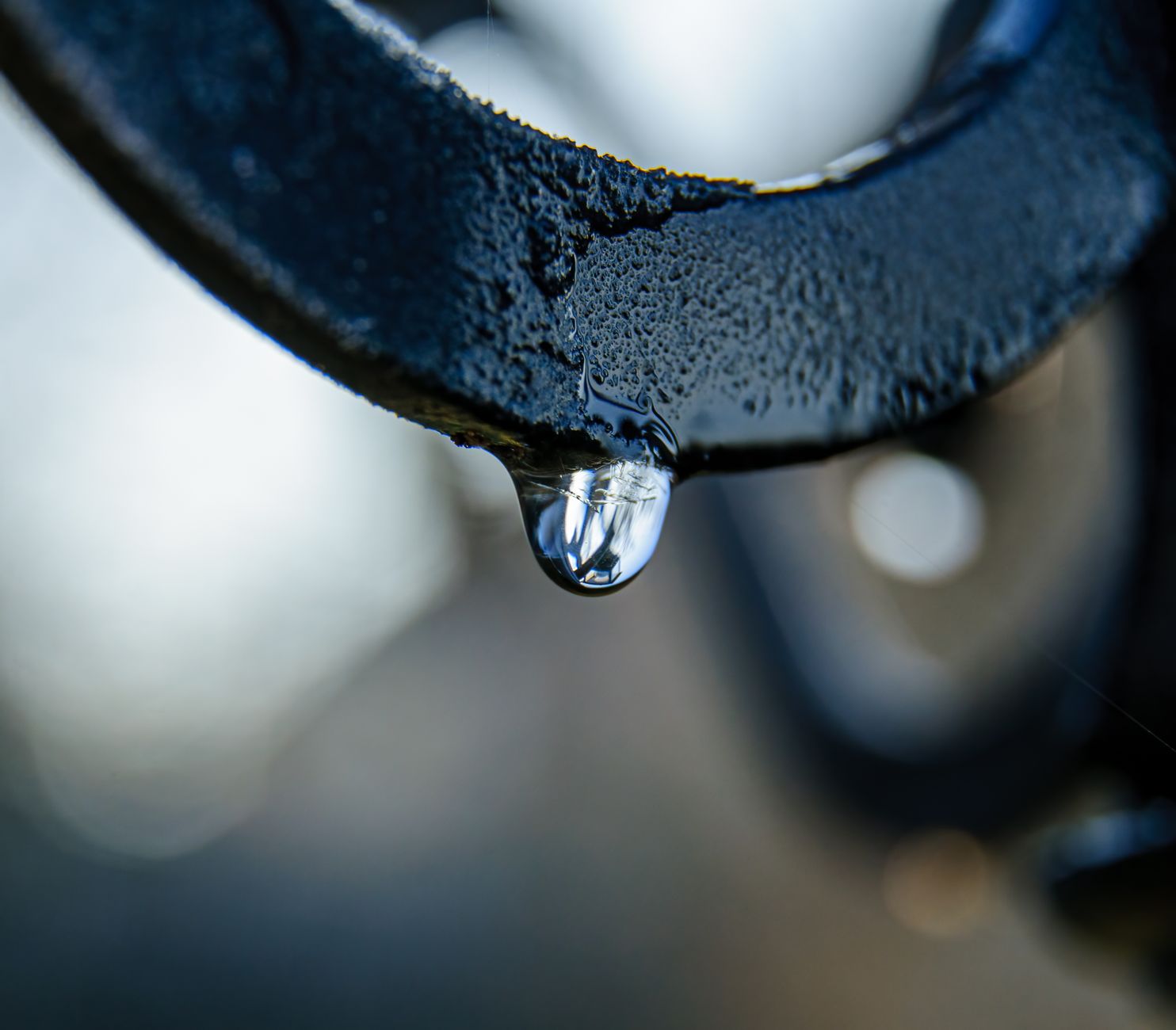 Macro shot of a dew drop hanging from a metal surface, reflecting light.